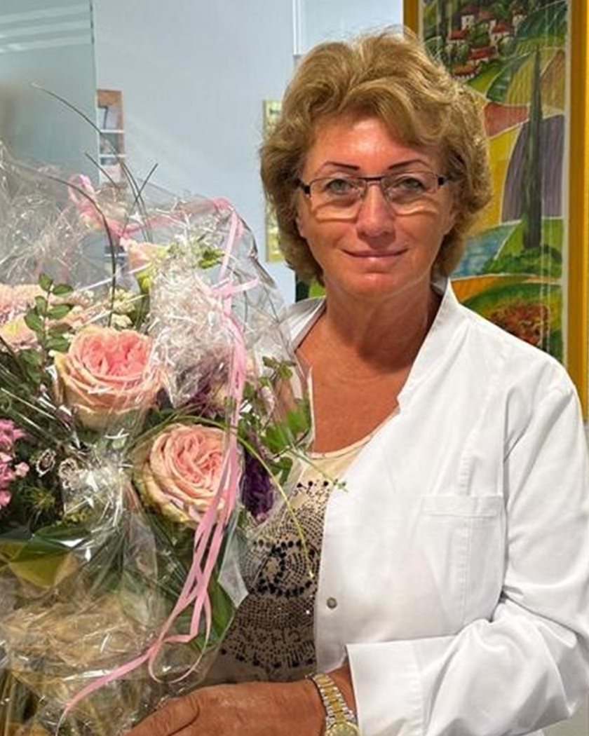 Dr. Lydia Vöhringer im weißen Kittel mit einem Blumenstrauß in der Praxis